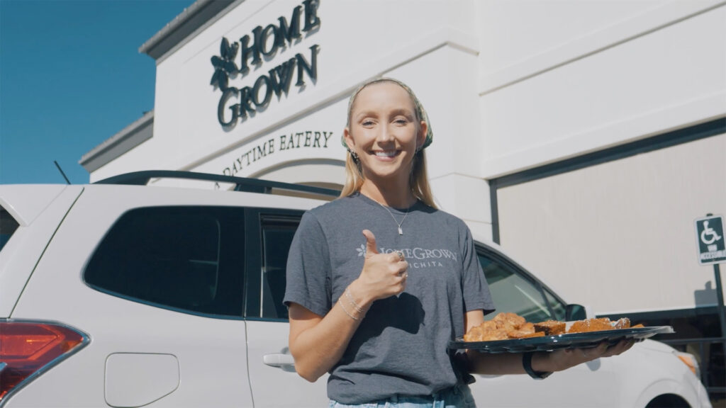 employee stands in front of restaurant, giving thumbs up